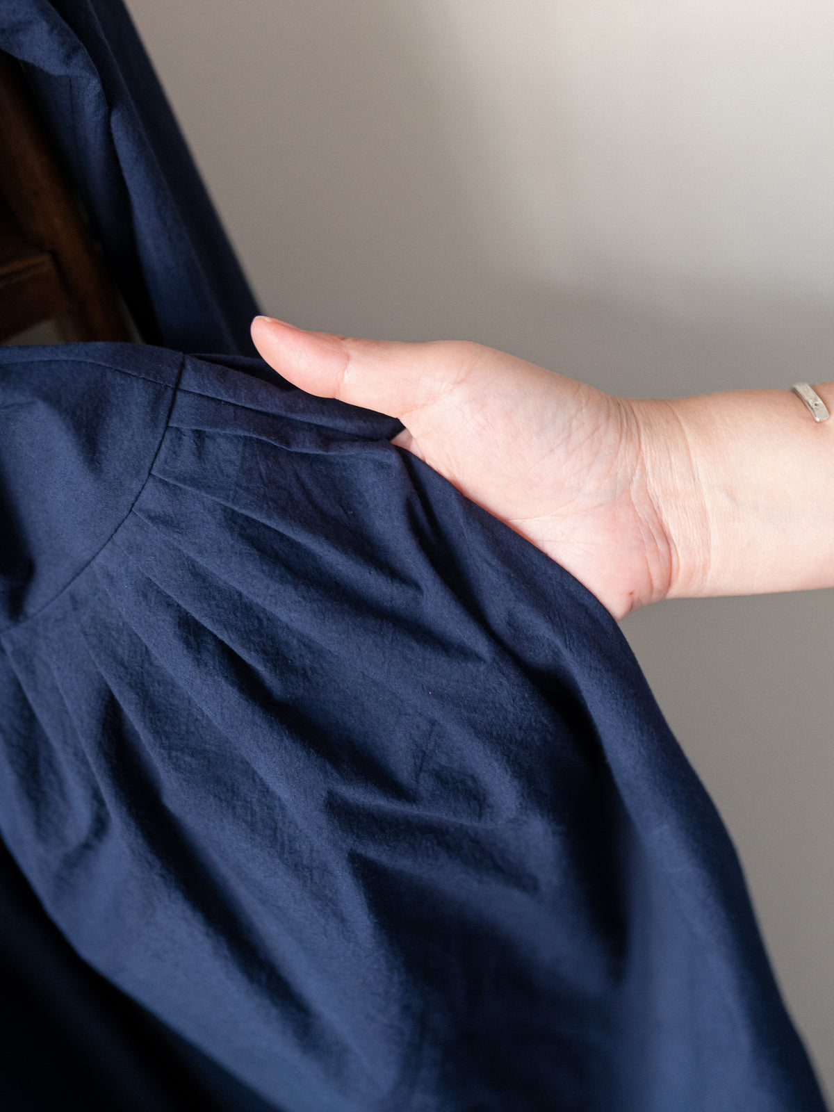 A close-up of a person's hand holding and showing the texture of a dark navy blue garment, likely a dress or long-sleeve top, against a neutral indoor background.